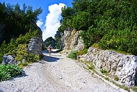 Eine Radfahrerin im Hochgebirge, die auf einer Schotterpiste durch einen Felsdurchbruch fhrt.